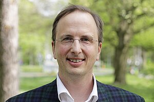 Ein Mann mit Brille, kurzem Haar und einem karierten Jackett.