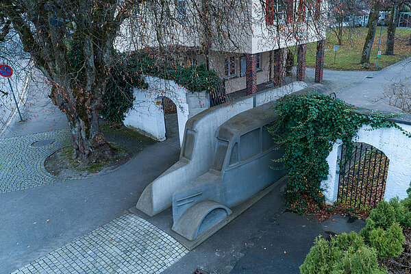 Das Denkmal der grauen Busse am ZfP-Standort Weissenau von einer Drohne aufgenommen, der graue Betonbus ist von schräg oben zu sehen, im Hintergrund das Gebäude Alte Pforte.
