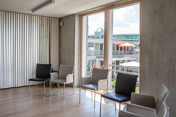 SINOVA Klinik in Friedrichshafen Zwei schwarze und zwei weiße Stühle stehen vor einer bodentiefen Fensterfront.
