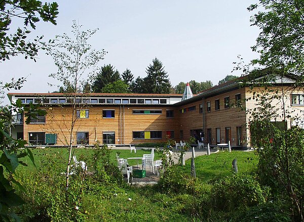 Holzvertäfeltes Gebäude inmitten einer grünen Landschaft. 