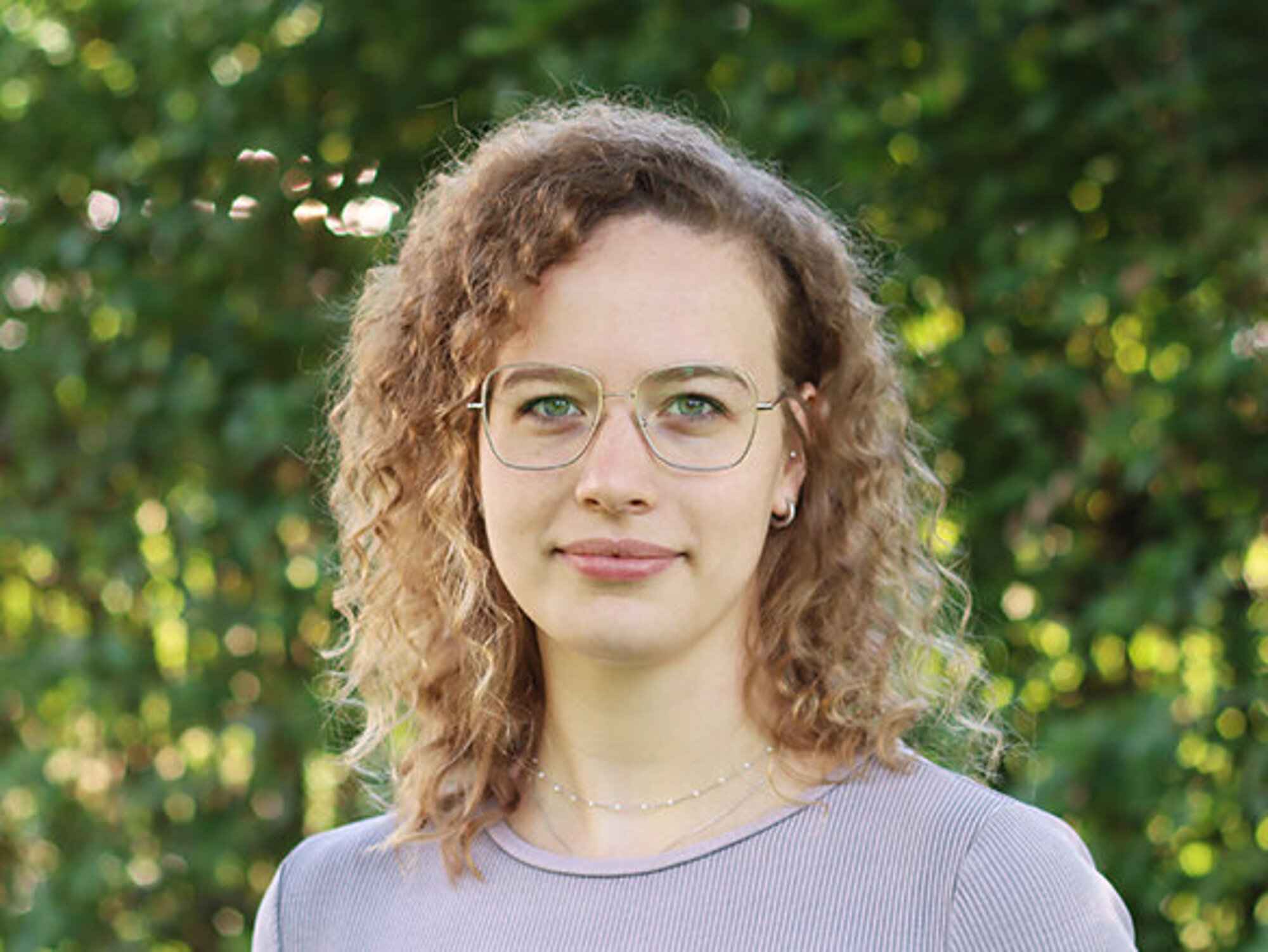 Portrait einer jungen Frau mit lockigen, blonden Haaren und Brille.