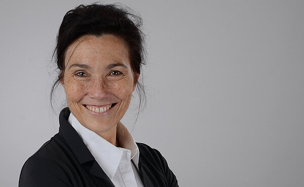 Eine dunkelhaarige Frau mit weißer Bluse, schwarzem Blazer und einer Hochsteckfrisur.