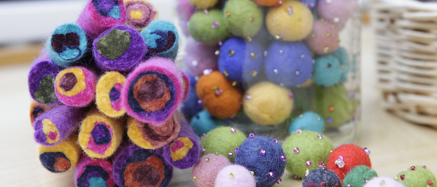 Man sieht eine Box mit bunten Filzkugeln. Daneben ist ein bunter Blumenstrauß aus Filz zu sehen.