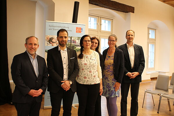 Drei Männer und drei Frauen stehen nebeneinander, im Hintergrund ist ein Banner mit dem Logo der Epilepsie-Akademie erkennbar. 