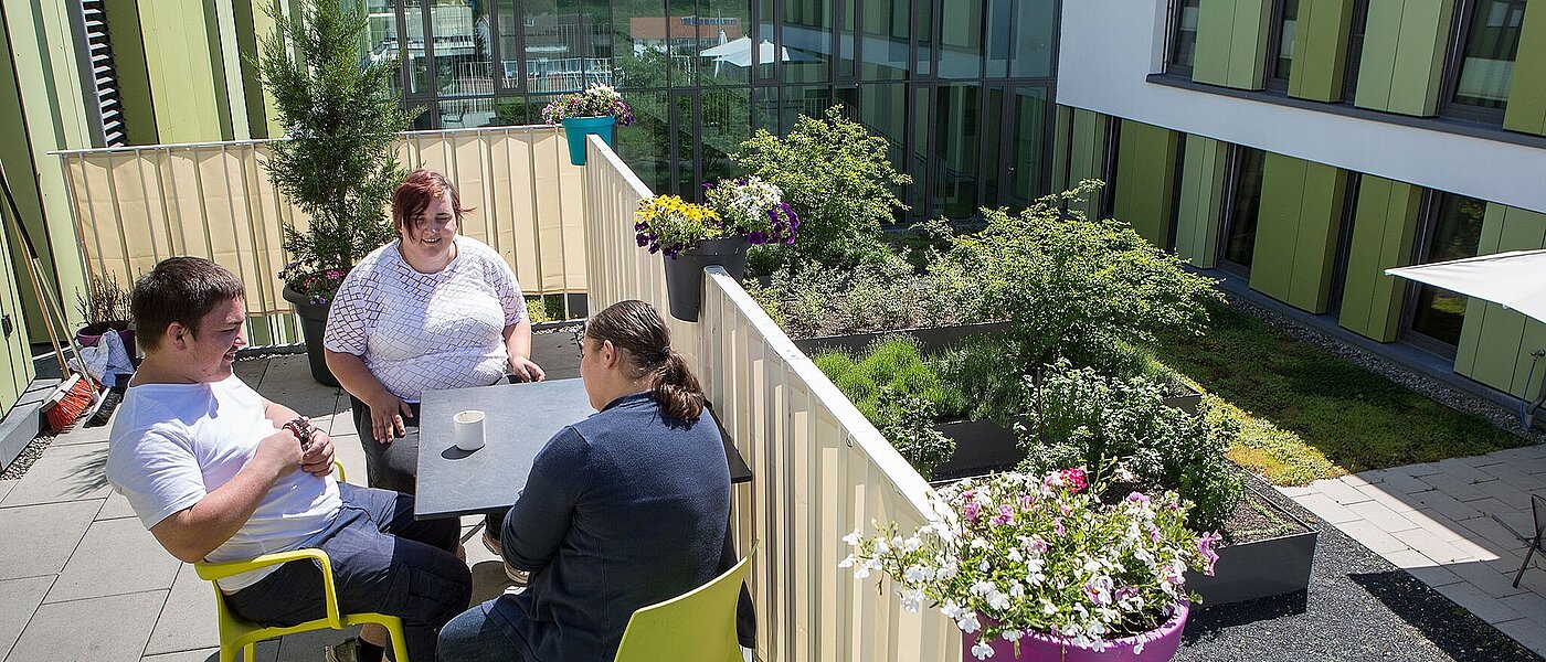 Drei Personen sitzen auf dem Balkon und unterhalten sich