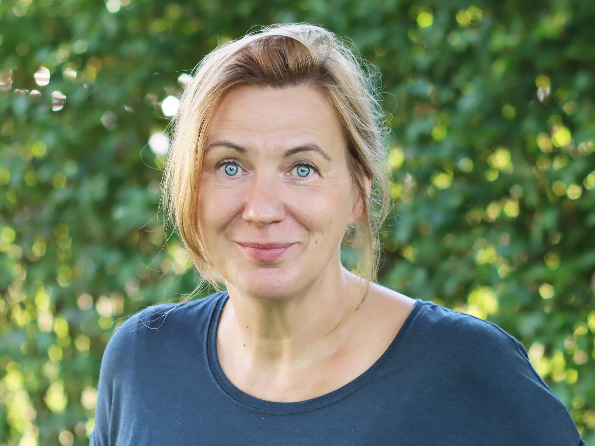 Porträt einer Frau mit hellen Augen und blondem, zurückgebundendem Haar.