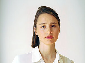 Eine junge Frau mit brünettem, glatten Haar und weißer Bluse. 