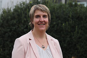 Eine blonde Frau mit kürzeren Haaren, weißer Bluse und roséfarbenem Blazer.