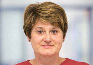 Porträtfoto einer Frau mit dunkelblonden kurzen Haaren. Sie trägt ein rotes Oberteil und schaut freundlich in die Kamera.