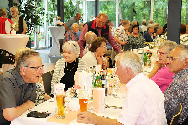 Viele ältere Menschen sitzen an festlich gedeckten Tischen und unterhalten sich.