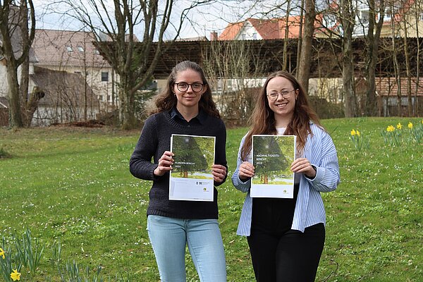 Zwei junge Frauen, beide mit Brille, halten den Nachhaltigkeitsbericht in den Händen.